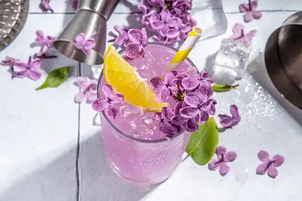 Lilac lemonade and lilac flowers with a lemon wedge in a glass.