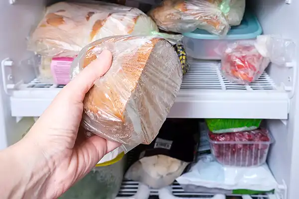 Half of a loaf of bread wrapped in plastic being put into a freezer, demonstrating how to freeze bread.