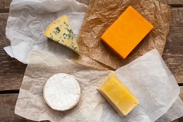 Four different cheeses on top of parchment paper, ready to be wrapped up and stored in the freezer.